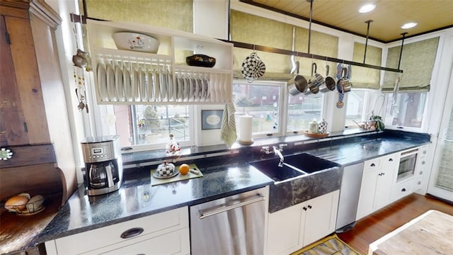 kitchen featuring stainless steel appliances, dark countertops, a sink, and white cabinetry