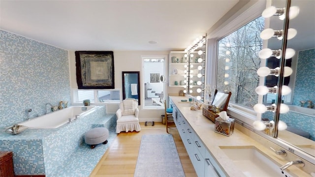 full bath featuring double vanity, a garden tub, a sink, and wood finished floors