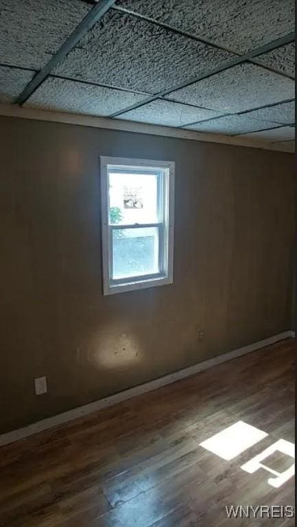 empty room featuring wood finished floors, a paneled ceiling, and baseboards