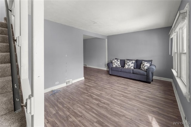 unfurnished living room featuring visible vents, stairway, baseboards, and wood finished floors