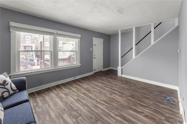 unfurnished living room featuring wood finished floors, a textured ceiling, baseboards, and stairs