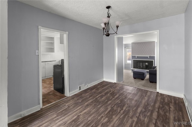 unfurnished dining area with a textured ceiling, a notable chandelier, dark wood-style flooring, baseboards, and a glass covered fireplace