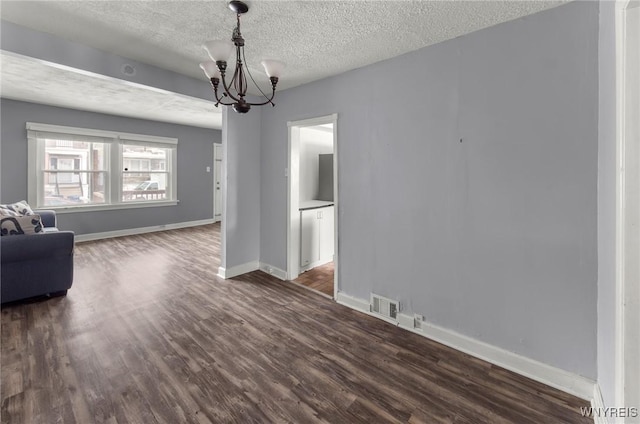 unfurnished living room with a textured ceiling, dark wood-type flooring, visible vents, baseboards, and an inviting chandelier