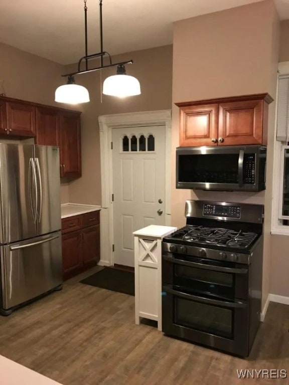 kitchen featuring stainless steel appliances, wood finished floors, light countertops, and baseboards