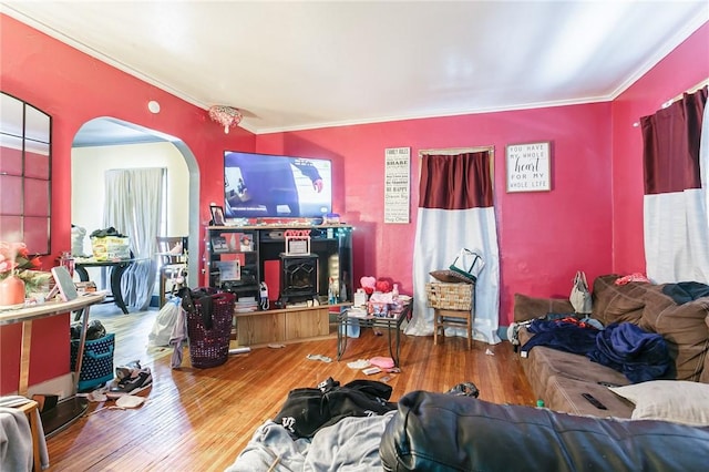 living room with a wood stove, ornamental molding, arched walkways, and wood finished floors