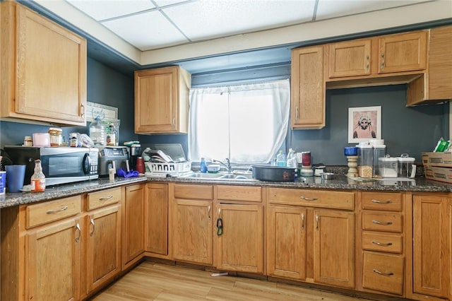 kitchen with dark stone counters, stainless steel microwave, a sink, and light wood-style flooring