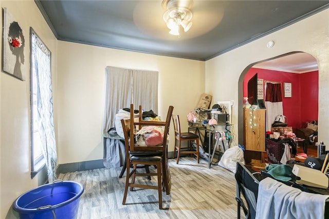 dining room featuring arched walkways, wood finished floors, a ceiling fan, baseboards, and ornamental molding