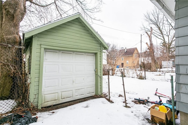 snow covered garage with fence and a detached garage