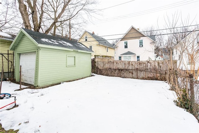 snowy yard with an outbuilding, a detached garage, and fence