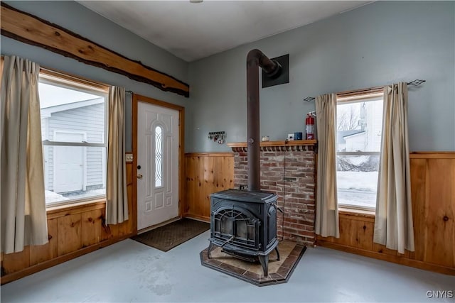 foyer entrance featuring a wood stove, a wainscoted wall, wood walls, and finished concrete flooring