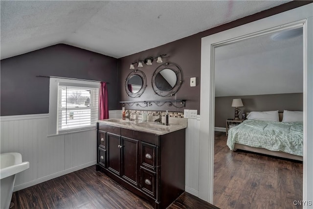 ensuite bathroom with a textured ceiling, vaulted ceiling, a sink, and wood finished floors