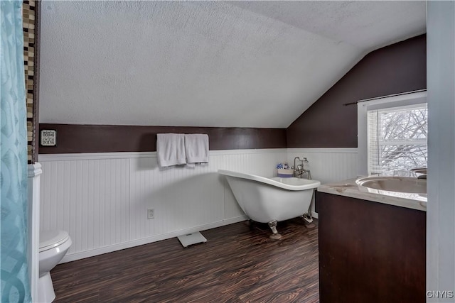 full bathroom featuring wainscoting, a soaking tub, wood finished floors, vaulted ceiling, and a textured ceiling