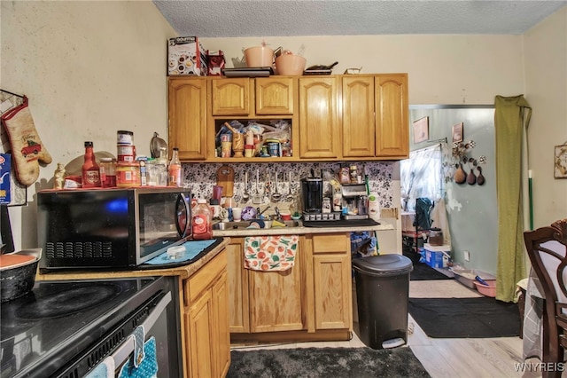 kitchen featuring a textured ceiling, black range with electric cooktop, wood finished floors, light countertops, and backsplash