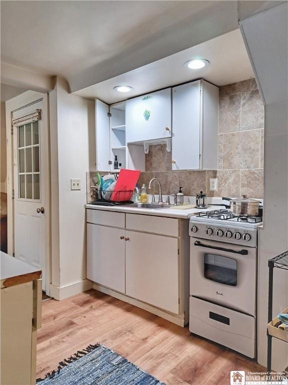 kitchen featuring range with gas stovetop, white cabinetry, backsplash, and light wood finished floors