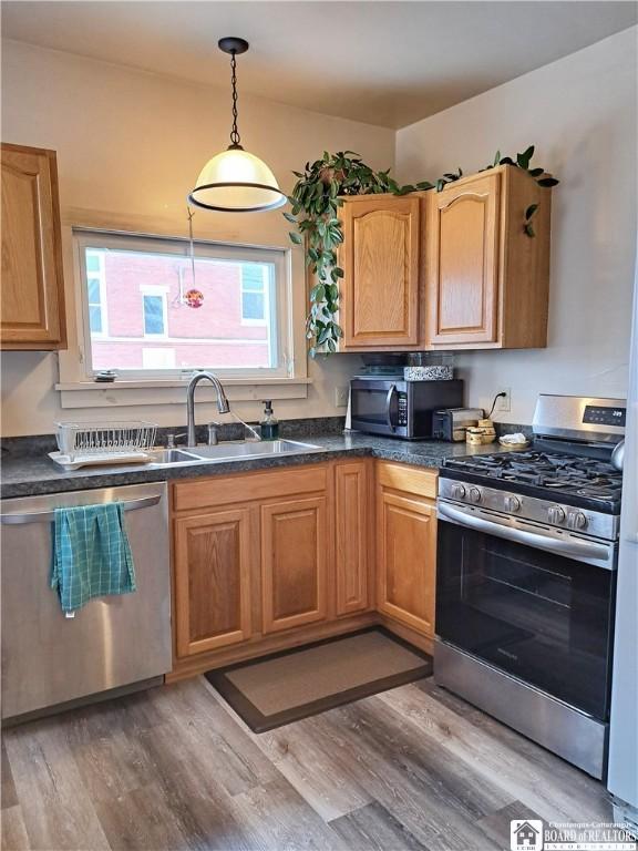 kitchen featuring dark countertops, hanging light fixtures, stainless steel appliances, light wood-style floors, and a sink