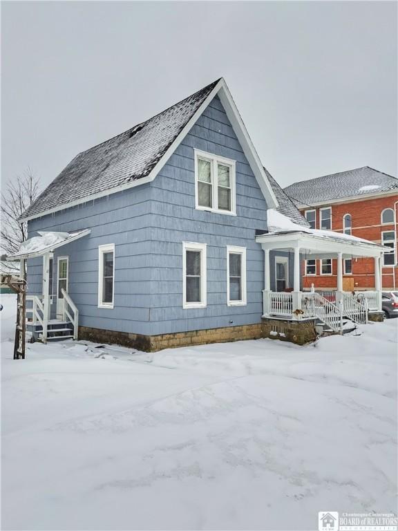 snow covered rear of property with a porch and roof with shingles