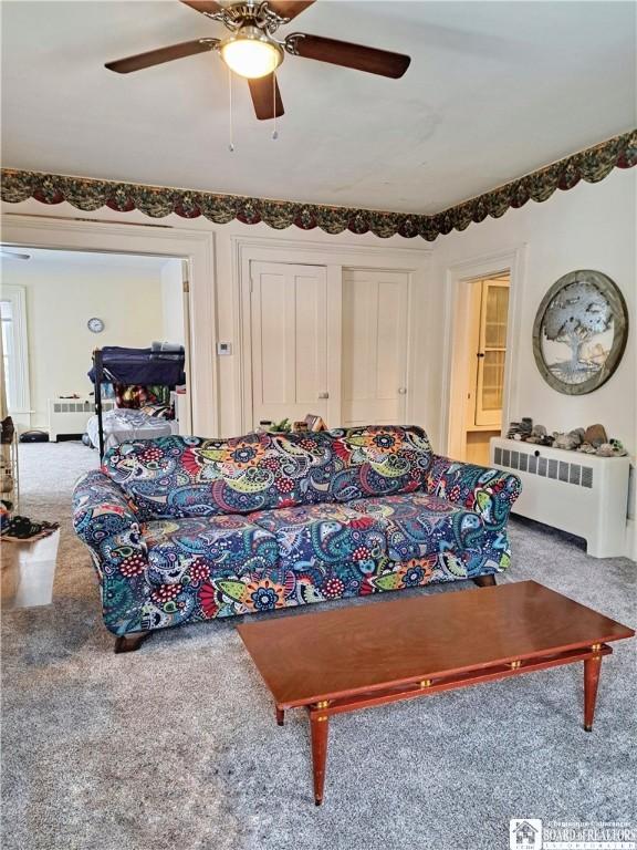 living area with ceiling fan, radiator heating unit, and carpet flooring