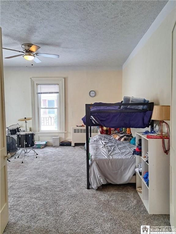 bedroom with a textured ceiling, ceiling fan, radiator heating unit, and carpet