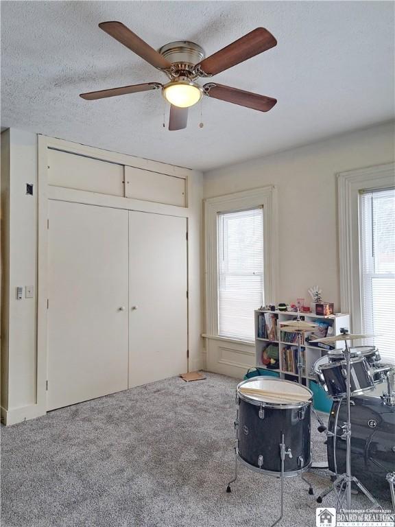 recreation room with a ceiling fan, carpet flooring, and a textured ceiling