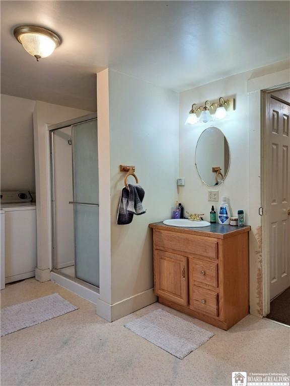 full bath featuring washer / clothes dryer, a stall shower, vanity, and baseboards