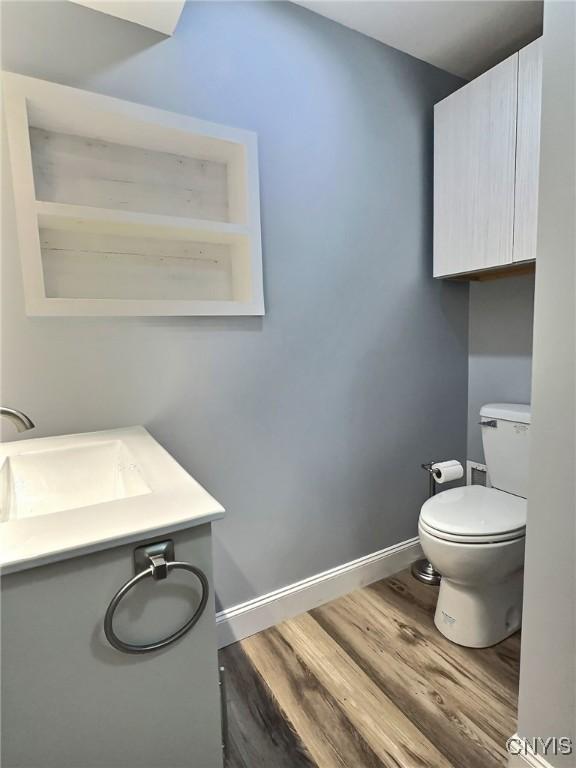 half bathroom with vanity, wood finished floors, toilet, and baseboards