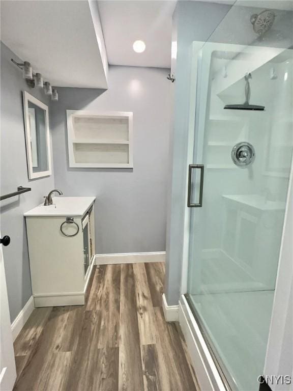 full bath featuring a stall shower, wood finished floors, vanity, and baseboards