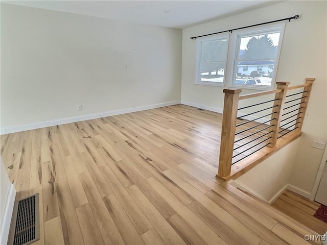 empty room with light wood finished floors, visible vents, and baseboards