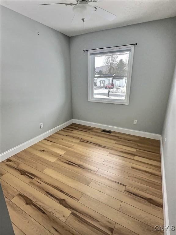 unfurnished room featuring baseboards, visible vents, a ceiling fan, and wood finished floors