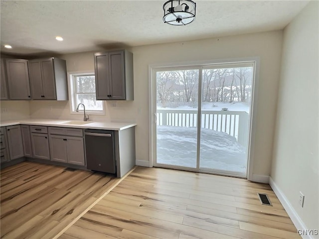 kitchen featuring visible vents, gray cabinetry, stainless steel dishwasher, a sink, and light wood-type flooring