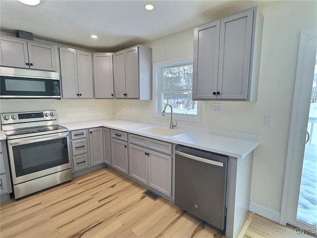 kitchen with gray cabinetry, a sink, light countertops, appliances with stainless steel finishes, and light wood-type flooring