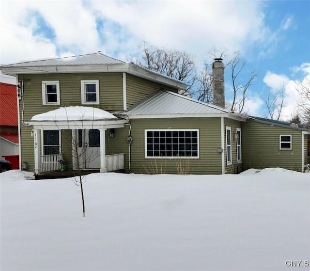 snow covered house with metal roof and a chimney