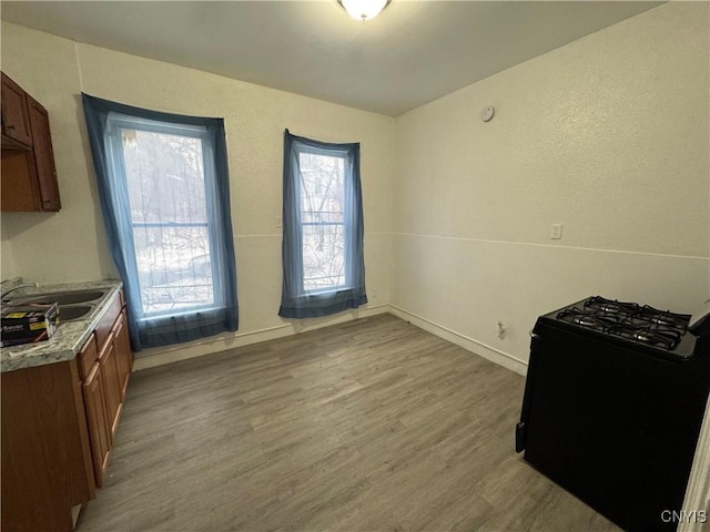 kitchen featuring light countertops, gas stove, a sink, light wood-type flooring, and baseboards