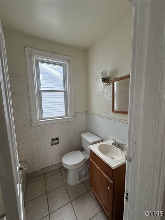 bathroom with tile patterned flooring, toilet, vanity, tile walls, and wainscoting