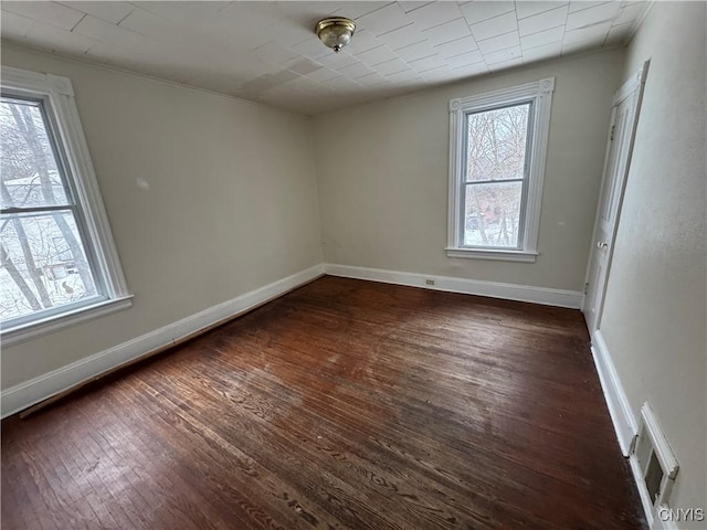 empty room with dark wood-type flooring, visible vents, and baseboards