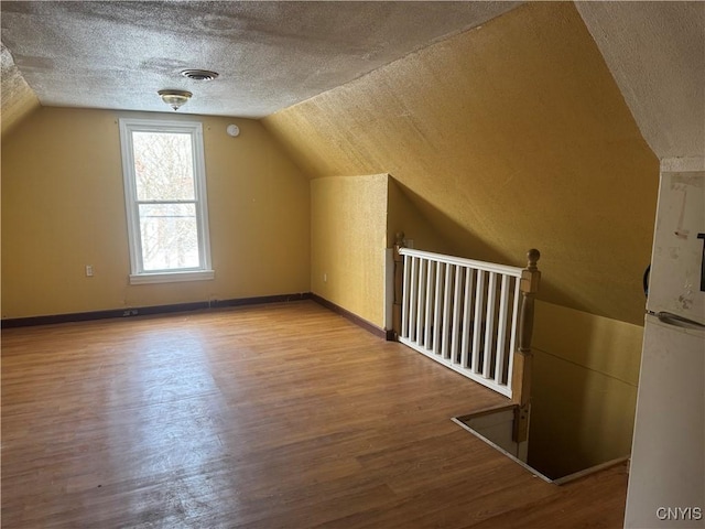 additional living space with visible vents, a textured ceiling, baseboards, and wood finished floors