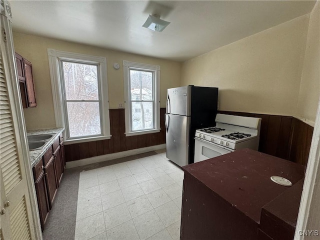 kitchen featuring freestanding refrigerator, wainscoting, a sink, wooden walls, and white range with gas stovetop