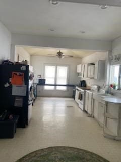 kitchen featuring white range with electric cooktop, a ceiling fan, freestanding refrigerator, light floors, and a sink