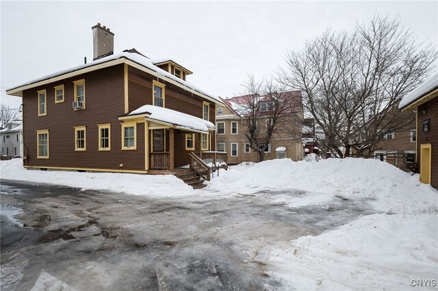 view of snow covered exterior with cooling unit and a chimney