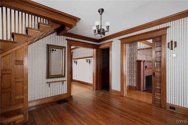 interior space with a chandelier, wood finished floors, visible vents, and wallpapered walls