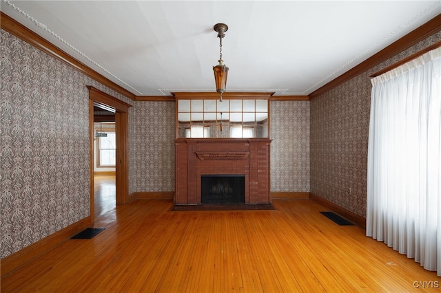 unfurnished living room with wood finished floors, a brick fireplace, visible vents, and wallpapered walls