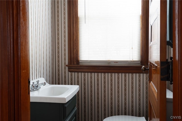 half bathroom with toilet, wallpapered walls, and vanity