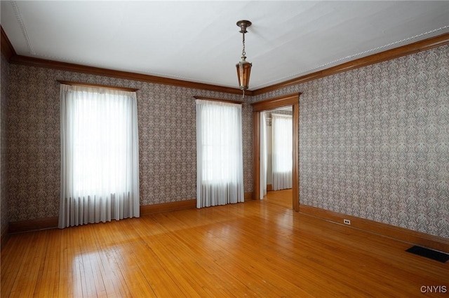 unfurnished room featuring wallpapered walls, visible vents, baseboards, light wood-style flooring, and crown molding