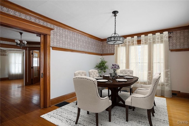 dining area featuring a notable chandelier, light wood-style flooring, ornamental molding, baseboards, and wallpapered walls