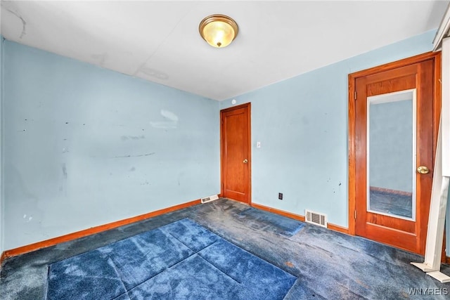 spare room with dark colored carpet, visible vents, and baseboards