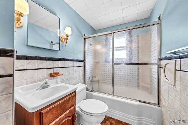 full bath featuring tile walls, toilet, wainscoting, combined bath / shower with glass door, and vanity