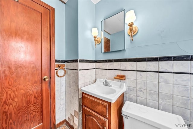 bathroom with tile walls, wainscoting, vanity, and toilet