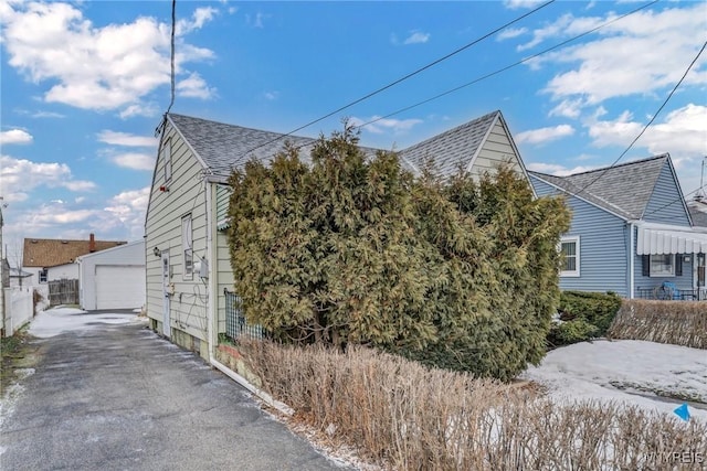 view of home's exterior featuring a garage, roof with shingles, fence, and an outdoor structure