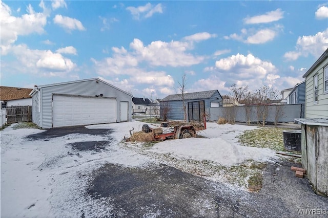 yard layered in snow featuring an outbuilding, central AC unit, fence, and a garage