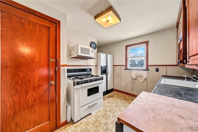 kitchen with white appliances, a sink, and wainscoting