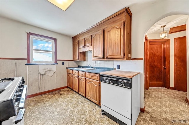 kitchen featuring arched walkways, range with two ovens, dishwasher, a wainscoted wall, and a sink